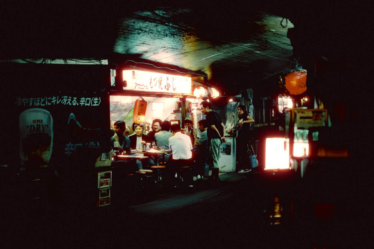 A late-night neighborhood gathering glowing beneath a shop sign.