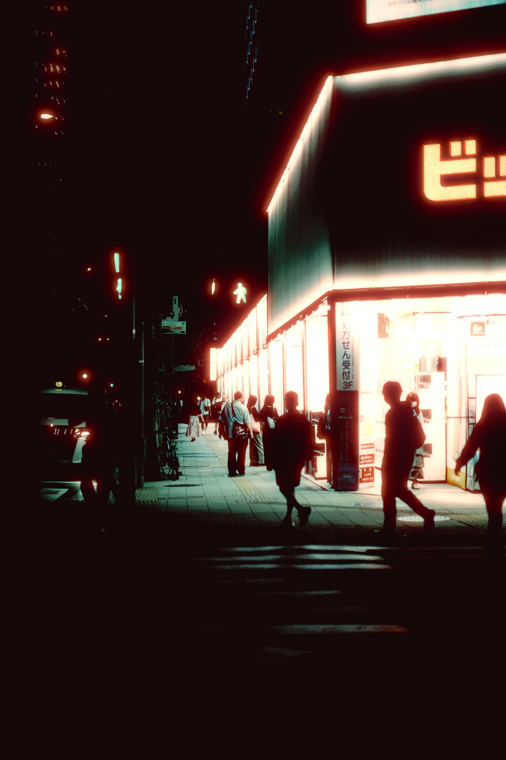 A brightly lit storefront and pedestrians at night.