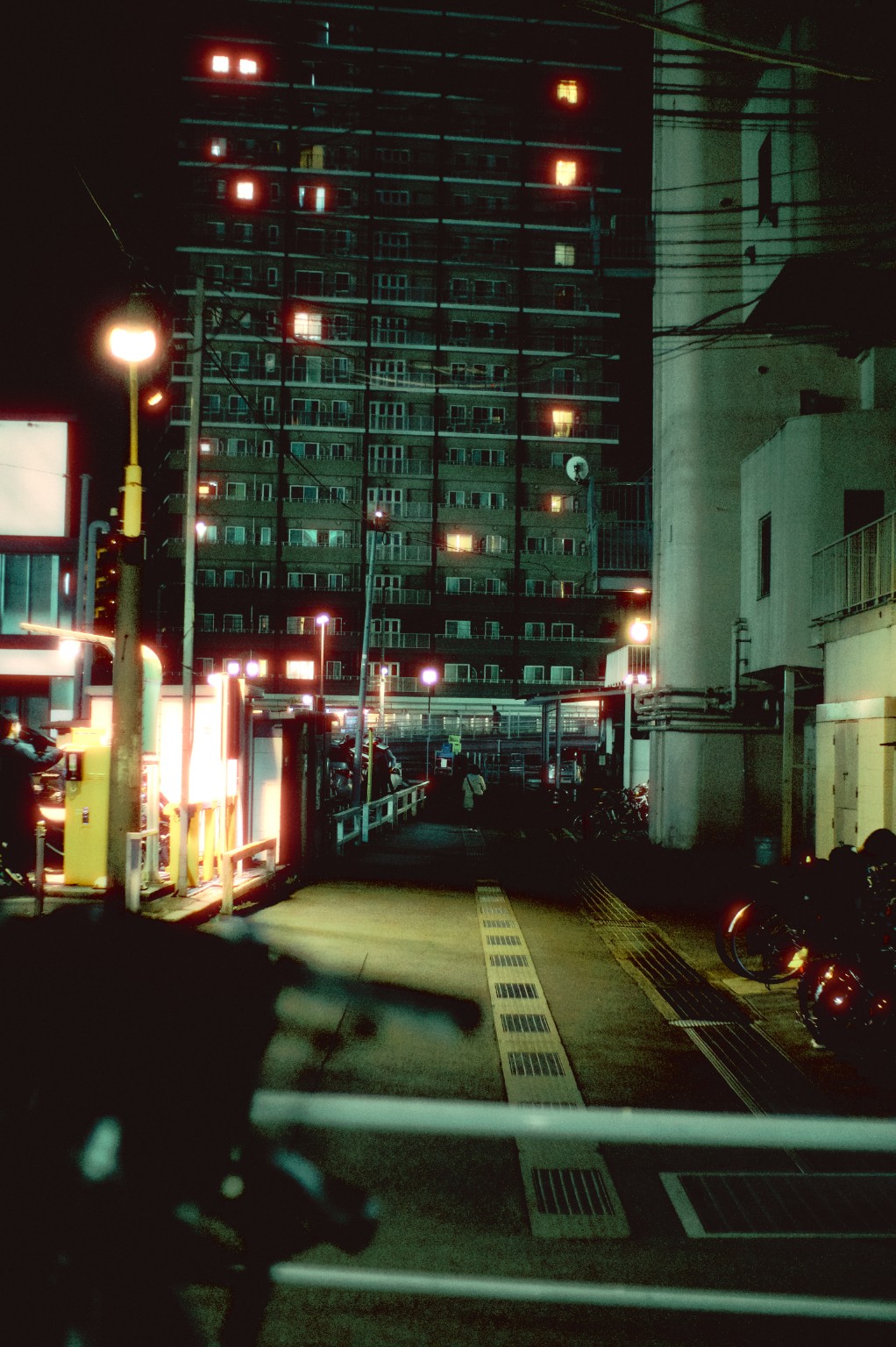 A nighttime city street with apartment lights and a glowing roadside sign.