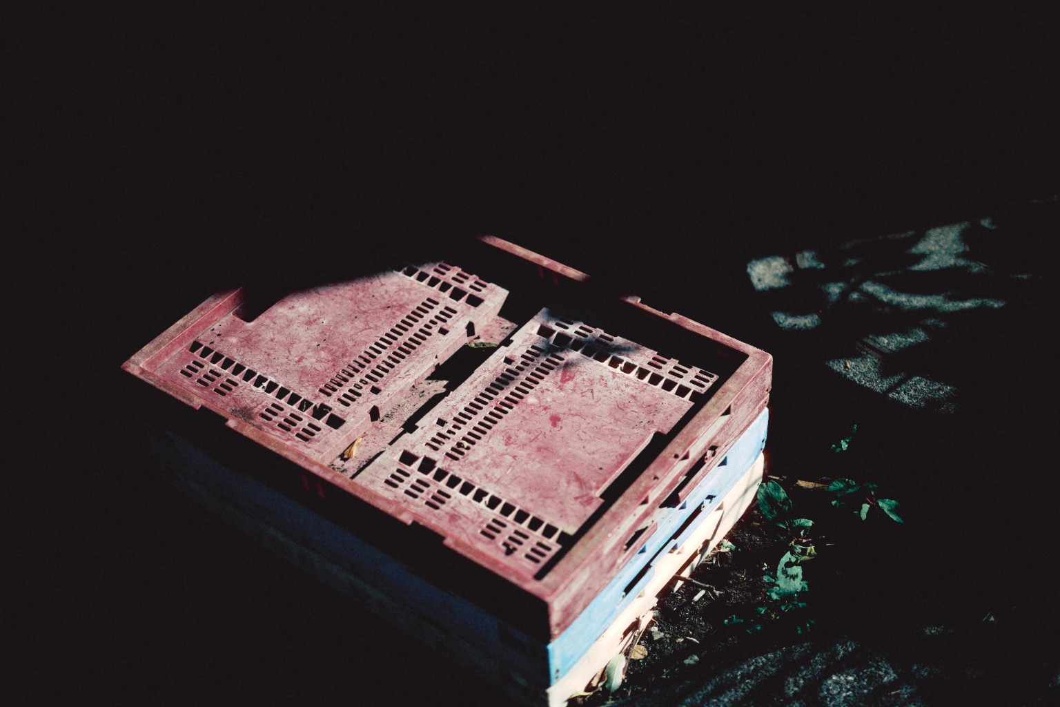A red produce crate in a pool of hard sunlight.